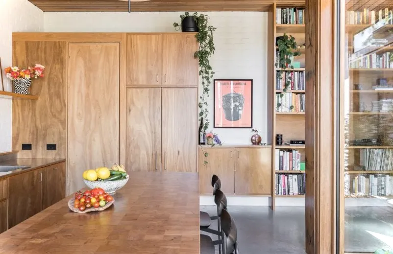 Cocina y comedor de planta abierta con piso de concreto, isla de cocina de madera con asientos y alacenas de madera.