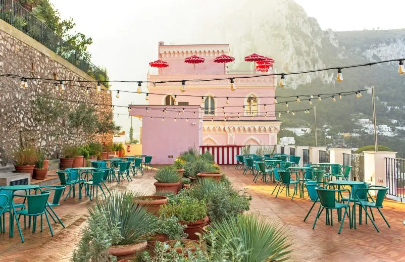 Terraza exterior con plantas en macetas y mesas de bar.