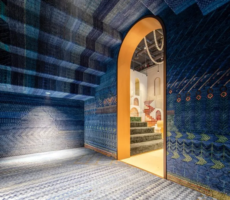 Foto de la sala Sapphire en la sala de exposición de Jaipur Rugs en Dubai que muestra alfombras con estampados azules que cubren las paredes, el piso y el techo, que también tiene forma escalonada.