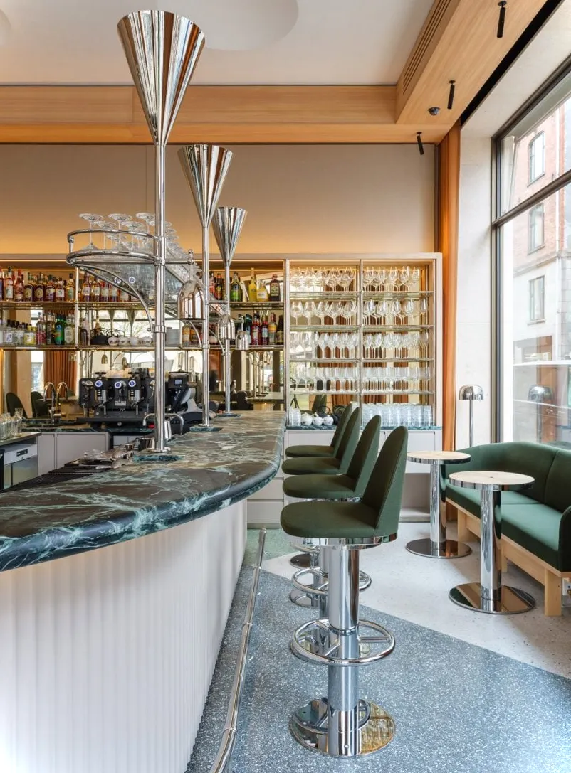 Bar restaurante con encimera de mármol verde, taburetes verdes y suelo de terrazo