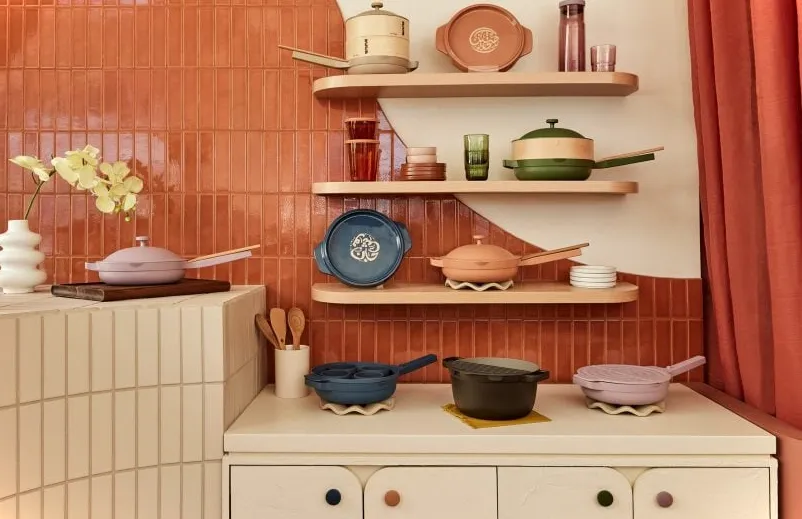 Utensilios de cocina expuestos en tres estantes y gabinetes debajo, contra una pared de azulejos