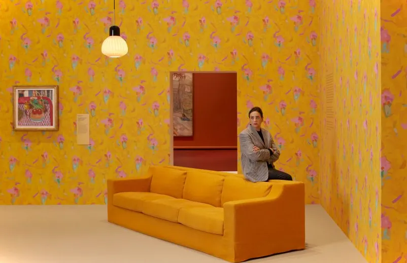 India Mahdavi recostada en un sofá amarillo en una galería amarilla