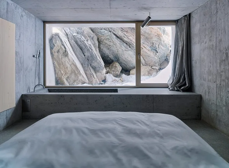 Dormitorio de hormigón con bañera rectangular junto a una ventana que da a las rocas