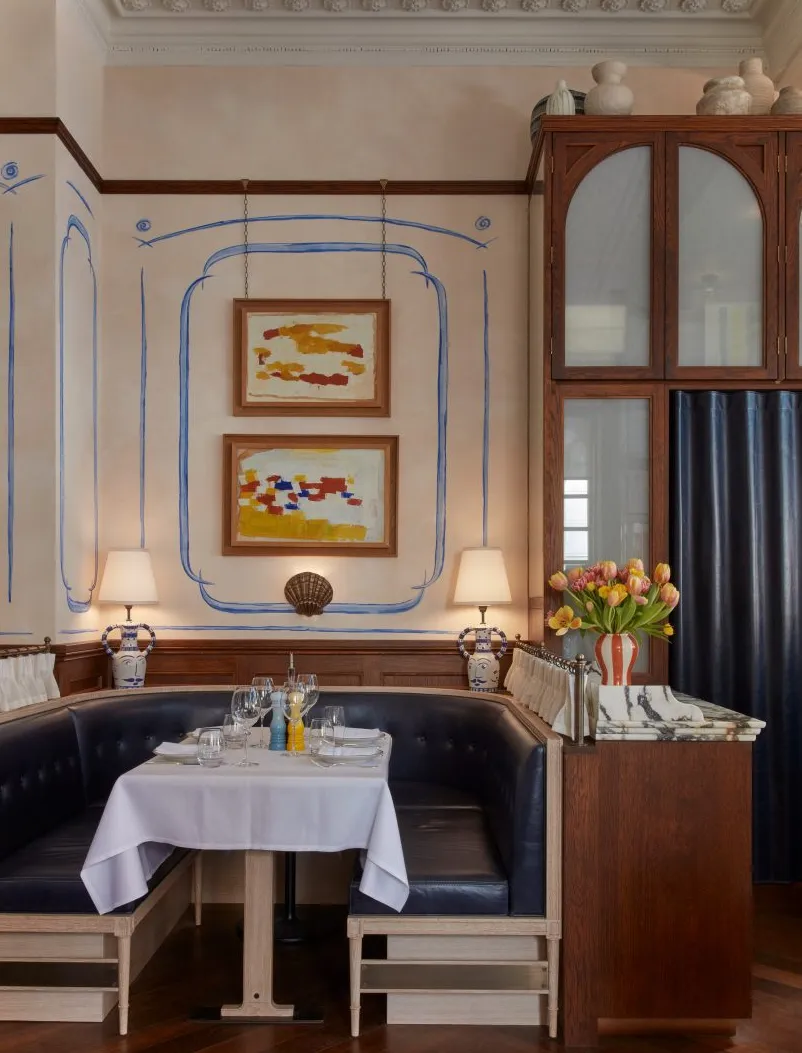 Interior del restaurante Socca con asientos en cabina color azul marino, paneles de pared de madera oscura y murales