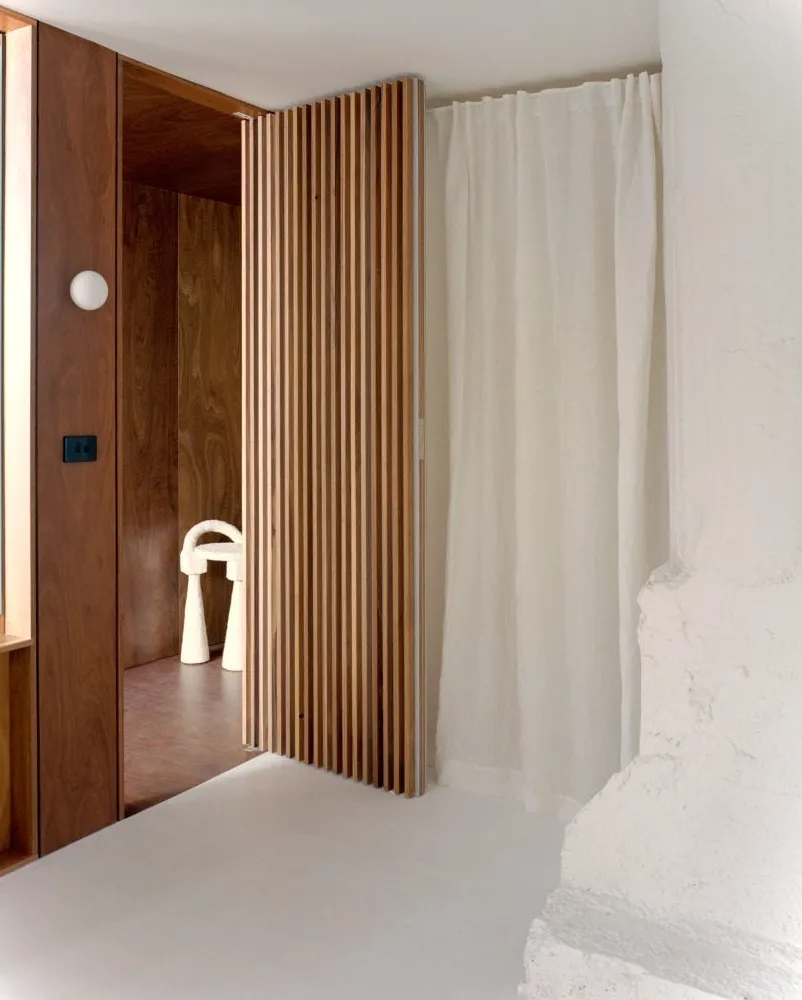 Puerta de madera con rejilla junto a cortinas transl煤cidas que acordonan un dormitorio