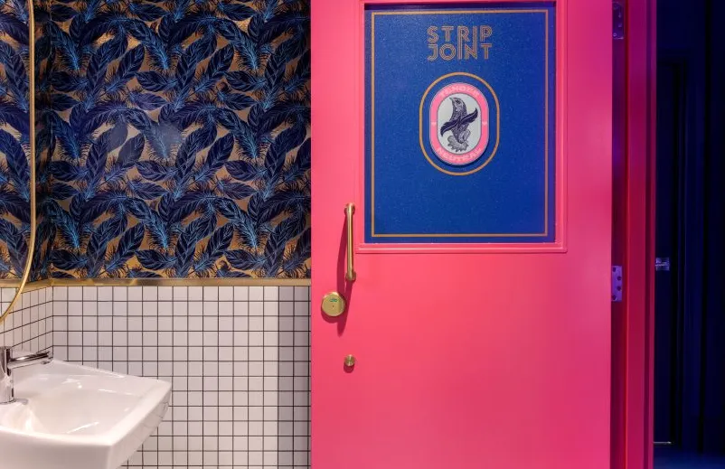 Cuarto de baño con papel tapiz de plumas y una puerta rosa brillante