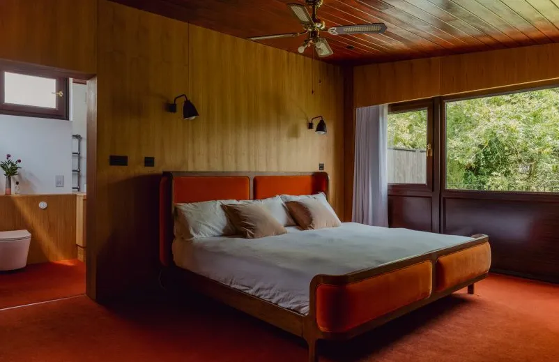 Dormitorio en Zero House con paredes con paneles de madera y alfombra naranja